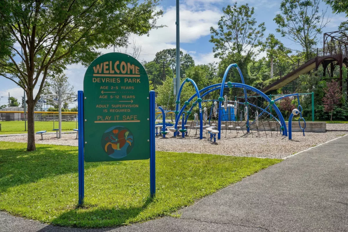 A park with a green sign and a playground in the background.
