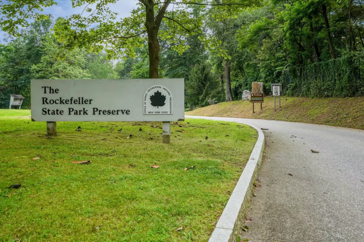 A driveway leading into a park next to a sign for The Rockefeller State Park Preserve.