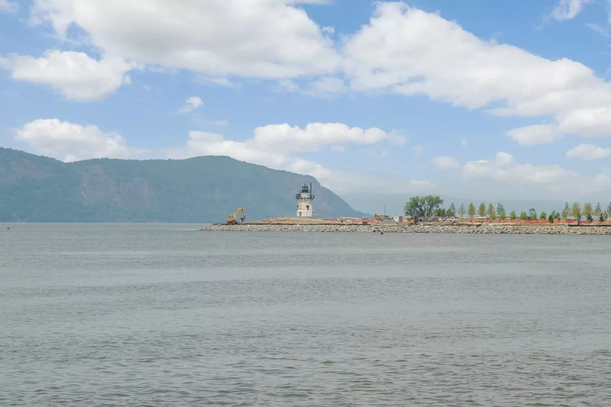 A river with a white lighthouse on a peninsula with a mountain in the background.