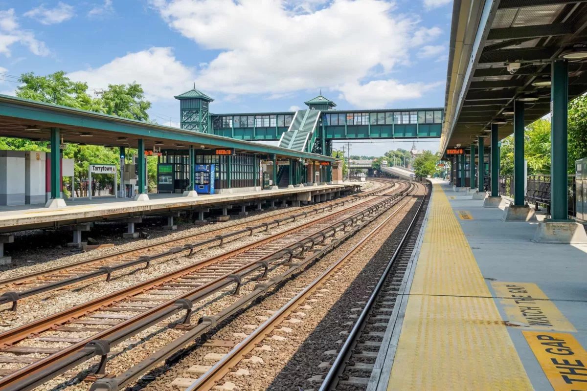 A train station and train track with a bridge over the tracks connecting to a station on the opposite side.